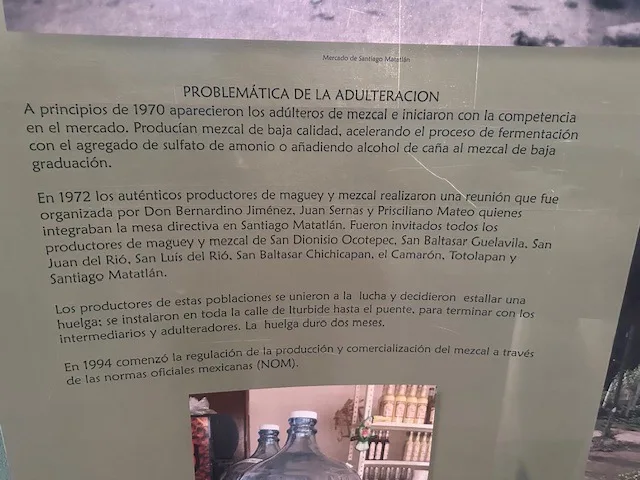 Museum placard at the Mercado de Santiago Matatlán reading "Problemática de la Adulteración," documenting how Don Bernardino Jiménez, Juan Sernas, and Pricsiliano Mateo organized the 1972 mezcalero strike against adulterators.